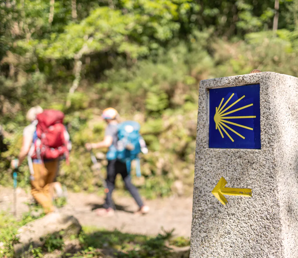 Peregrinos del Camino de Santiago junto a un mojón con la concha jacobea